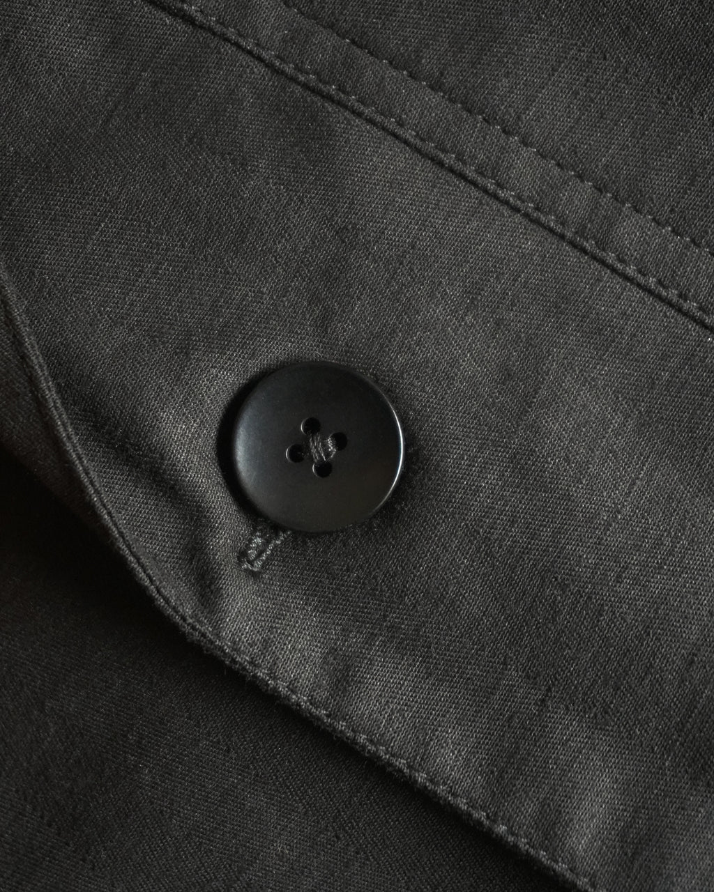 Close-up of MAYED black herringbone fabric and button detail.
