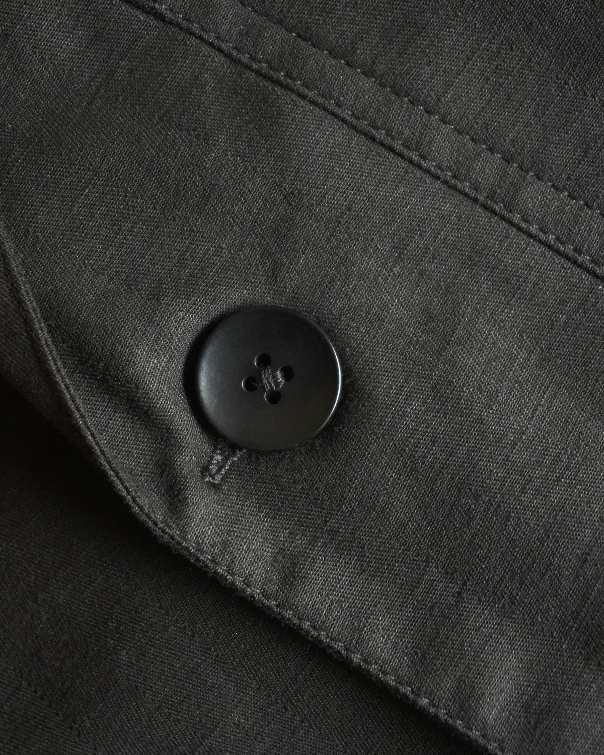 Close-up of MAYED black herringbone fabric and button detail.
