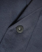 Alt text:
Detail of MAYED dark navy Candiani denim chore jacket showing fabric, seam and black tack button