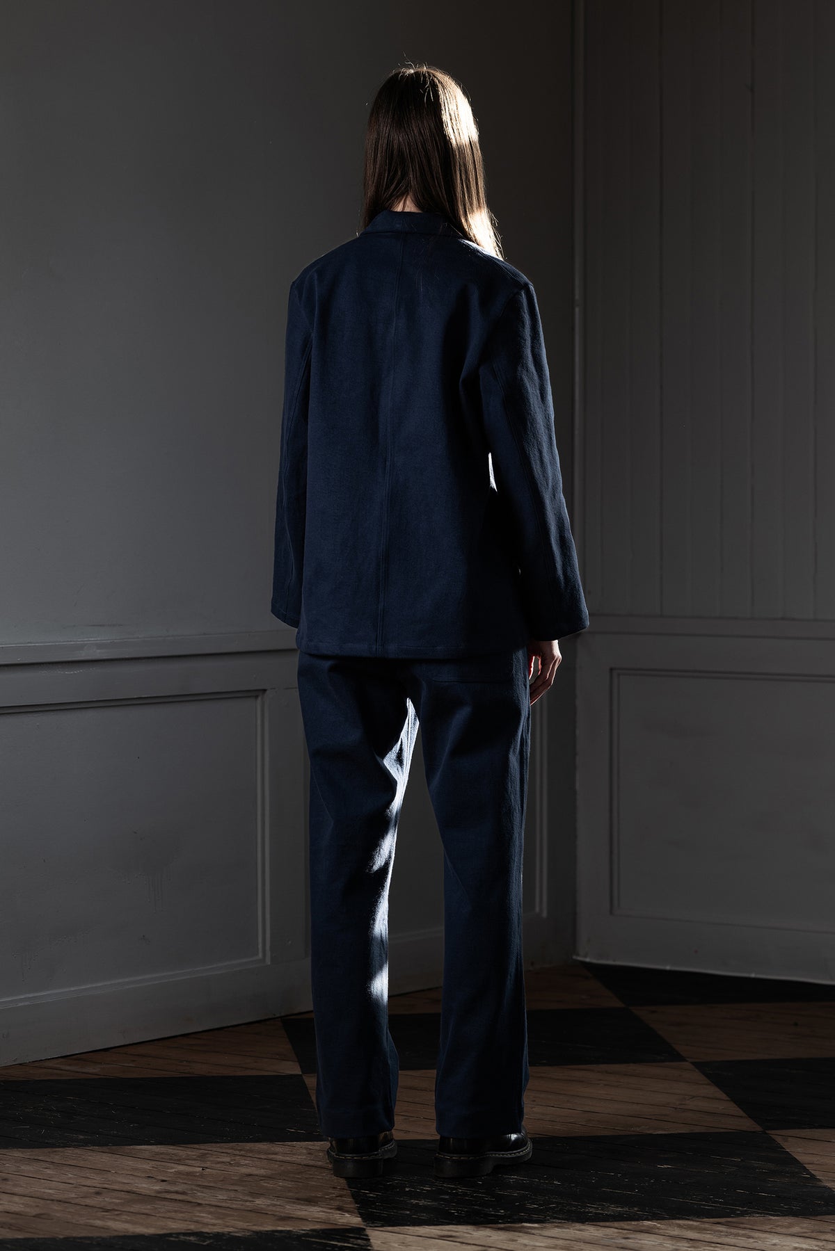 Back view of woman wearing MAYED dark navy Candiani denim chore jacket and matching trousers