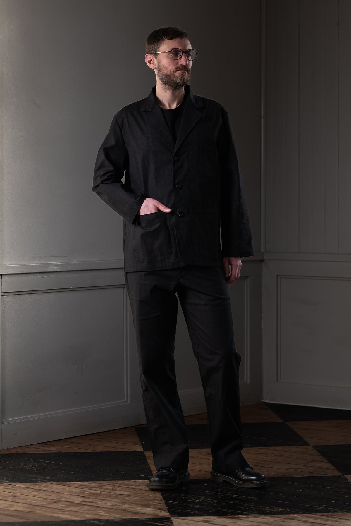 Man wearing MAYED black herringbone straight-leg trousers with matching chore jacket.