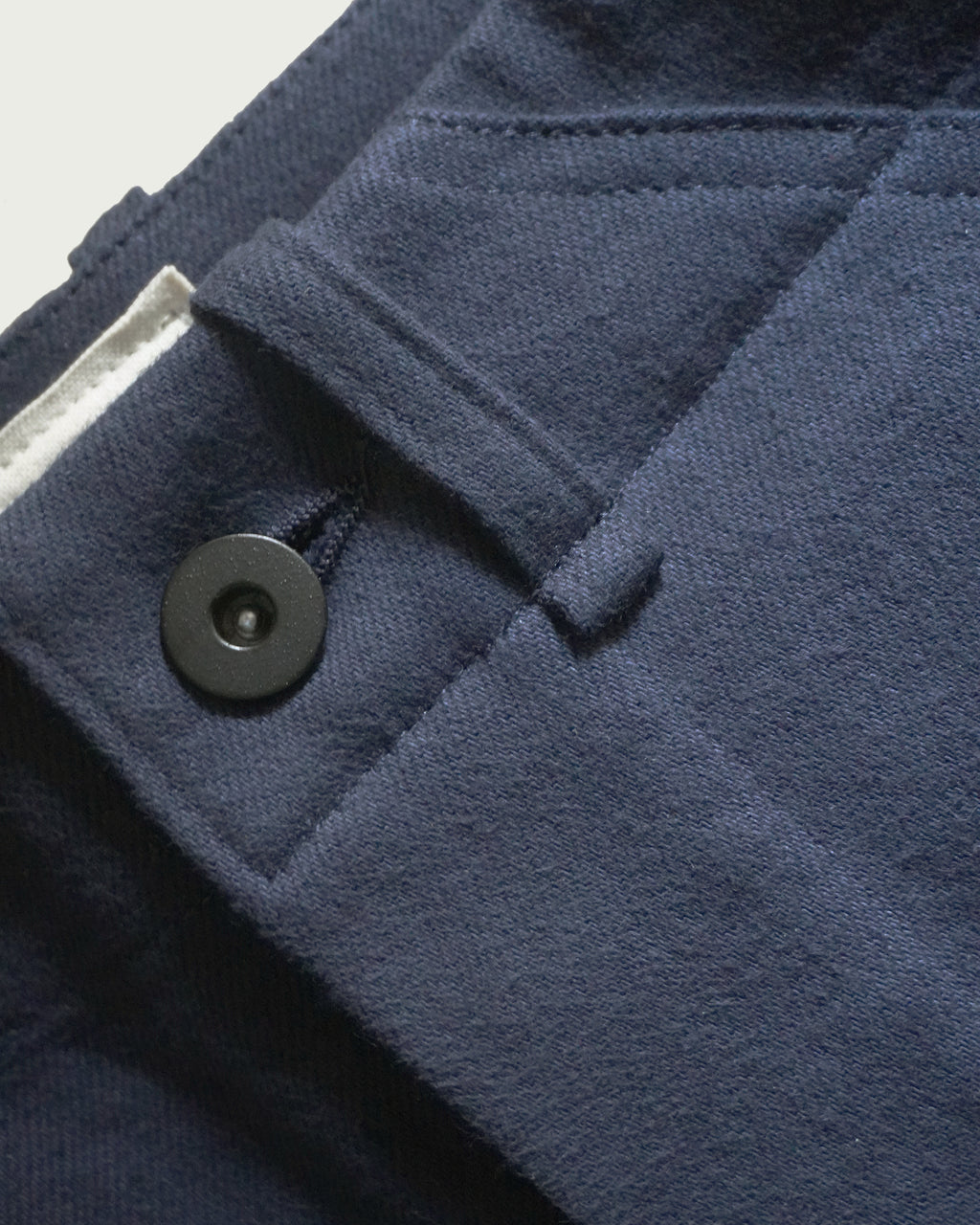 Detail of MAYED dark navy Candiani denim trousers showing waistband, belt loop and black tack button