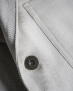 Detail of ecru Candiani denim and metal button on MAYED straight-leg trousers.