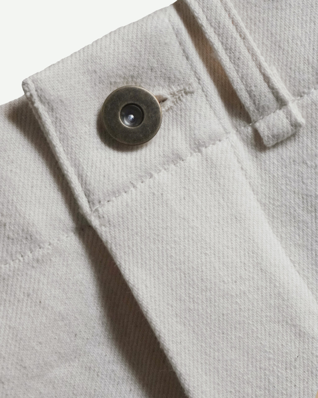 Close-up of MAYED women’s ecru Candiani denim trousers, showing waistband, belt loop and metal button detail.